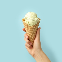 Photo of Woman holding waffle cone with delicious ice cream on light blue background, closeup