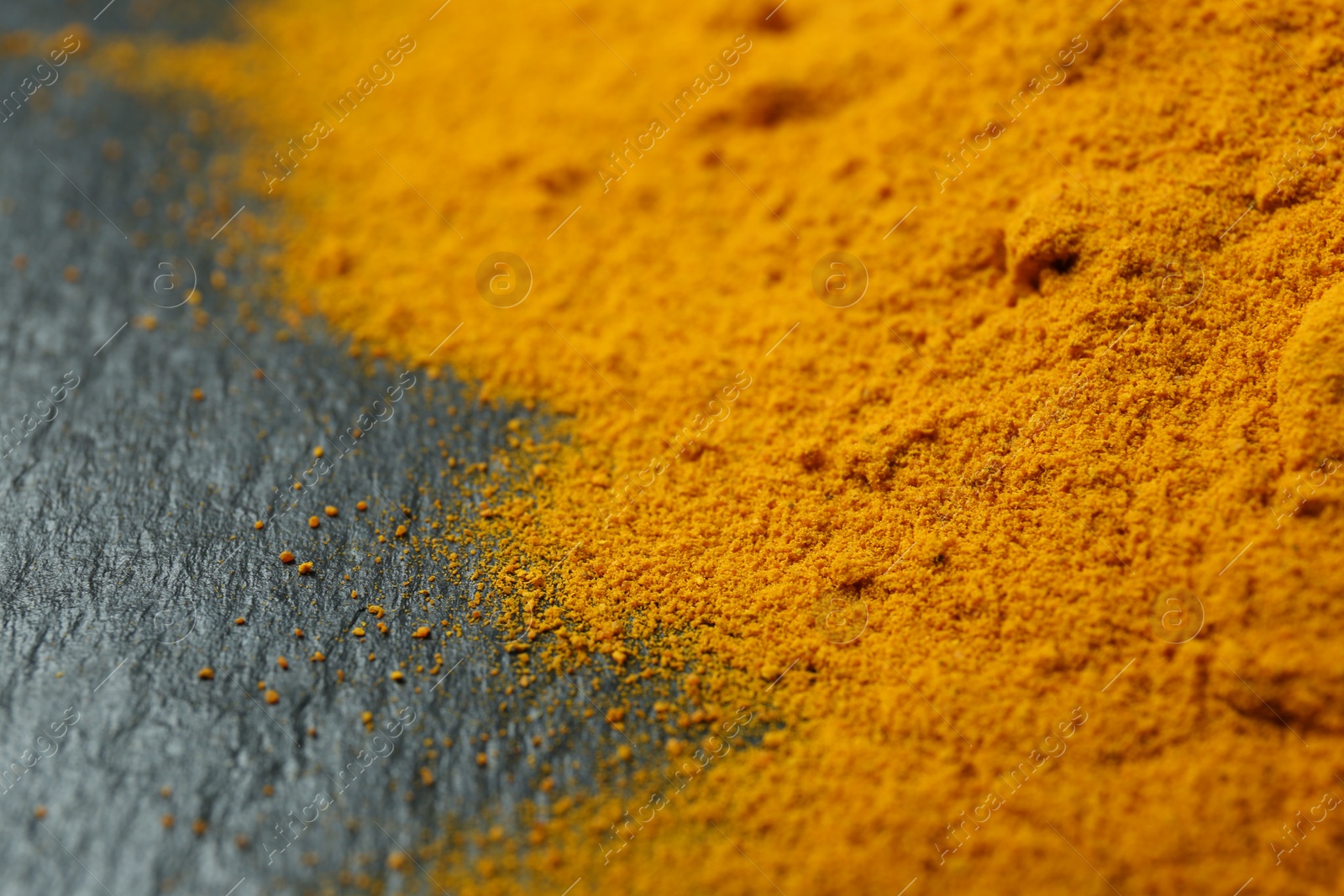 Photo of Turmeric powder on black textured table, closeup