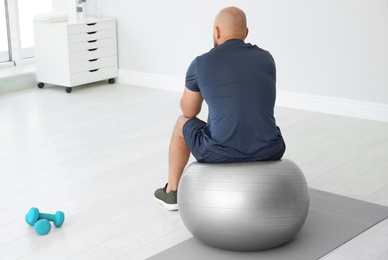 Tired overweight man sitting on fitness ball in gym