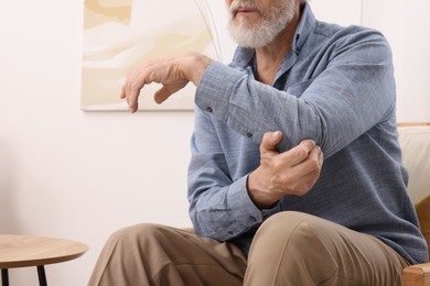 Photo of Senior man suffering from pain in his elbow at home, closeup. Arthritis symptoms