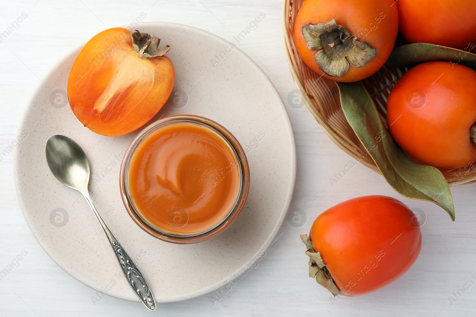 Photo of Delicious persimmon jam in glass jar served on white wooden table, flat lay