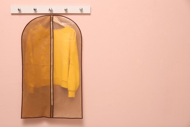Photo of Garment bag with sweatshirt hanging on light wall. Space for text