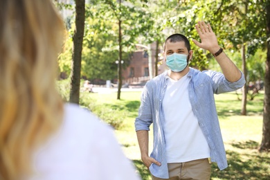 Photo of Man in protective face mask saying hello outdoors. Keeping social distance during coronavirus pandemic