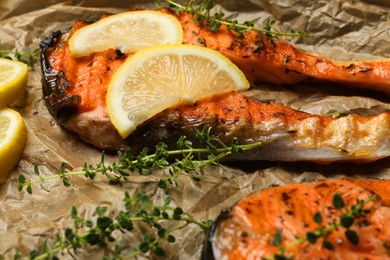 Photo of Tasty grilled salmon steaks, lemon slices and thyme on parchment paper, closeup