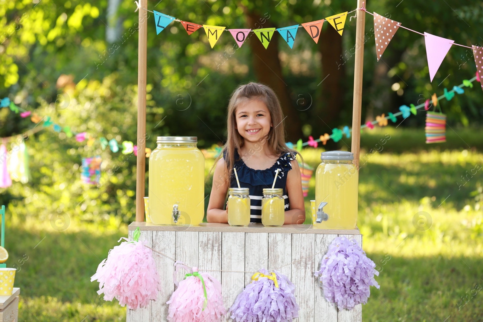 Photo of Cute little girl at lemonade stand in park. Summer refreshing natural drink