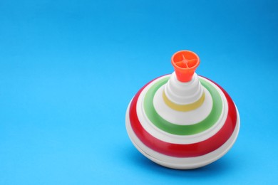 One bright spinning top on light blue background, space for text. Toy whirligig