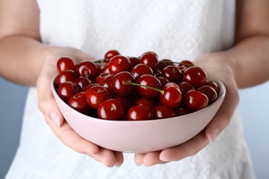 Photo of Woman holding bowl with ripe cherries, closeup