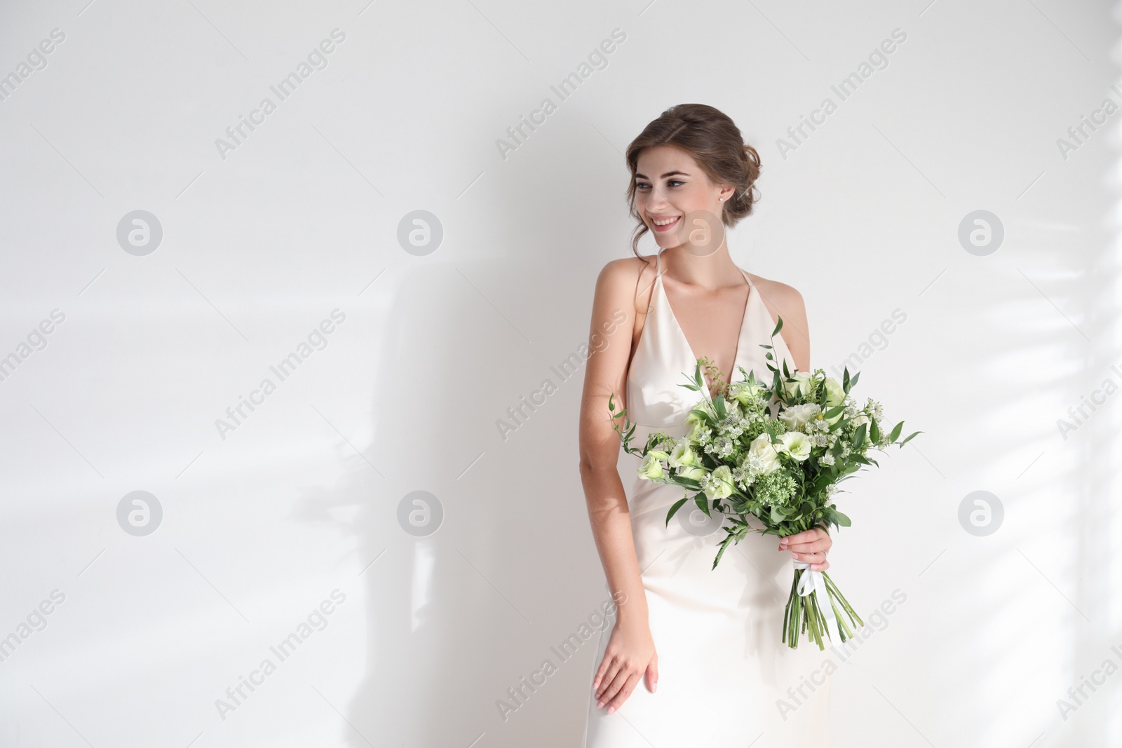 Photo of Young bride wearing wedding dress with beautiful bouquet on light background. Space for text