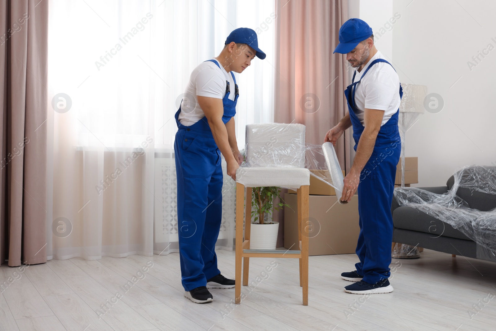 Photo of Workers wrapping chair in stretch film indoors. Space for text