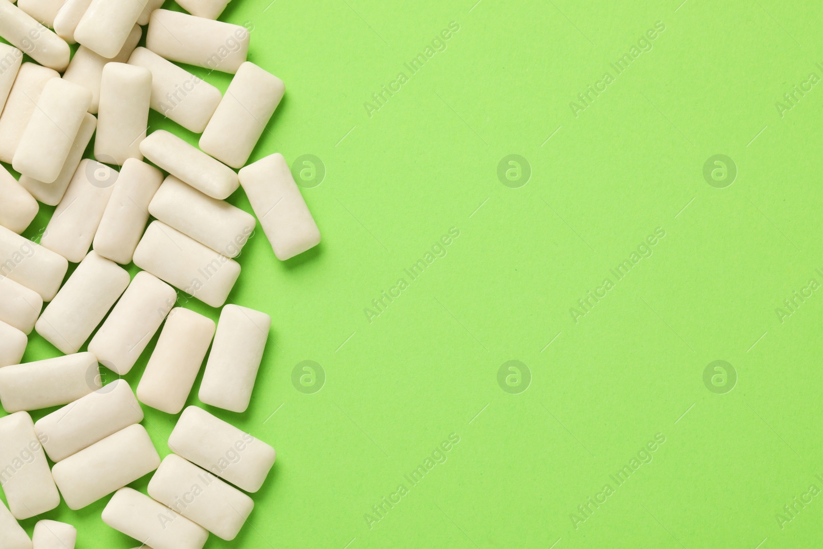 Photo of Many chewing gum pieces on green background, flat lay. Space for text