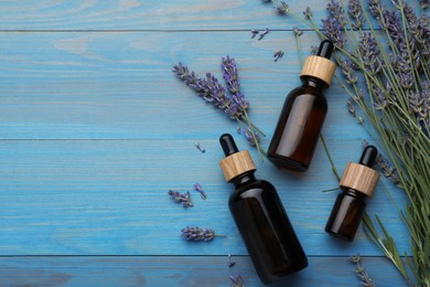 Photo of Bottles of essential oil and lavender flowers on light blue wooden table, flat lay. Space for text