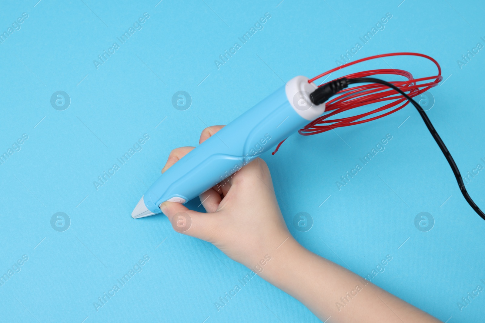 Photo of Boy drawing with stylish 3D pen on light blue background, top view