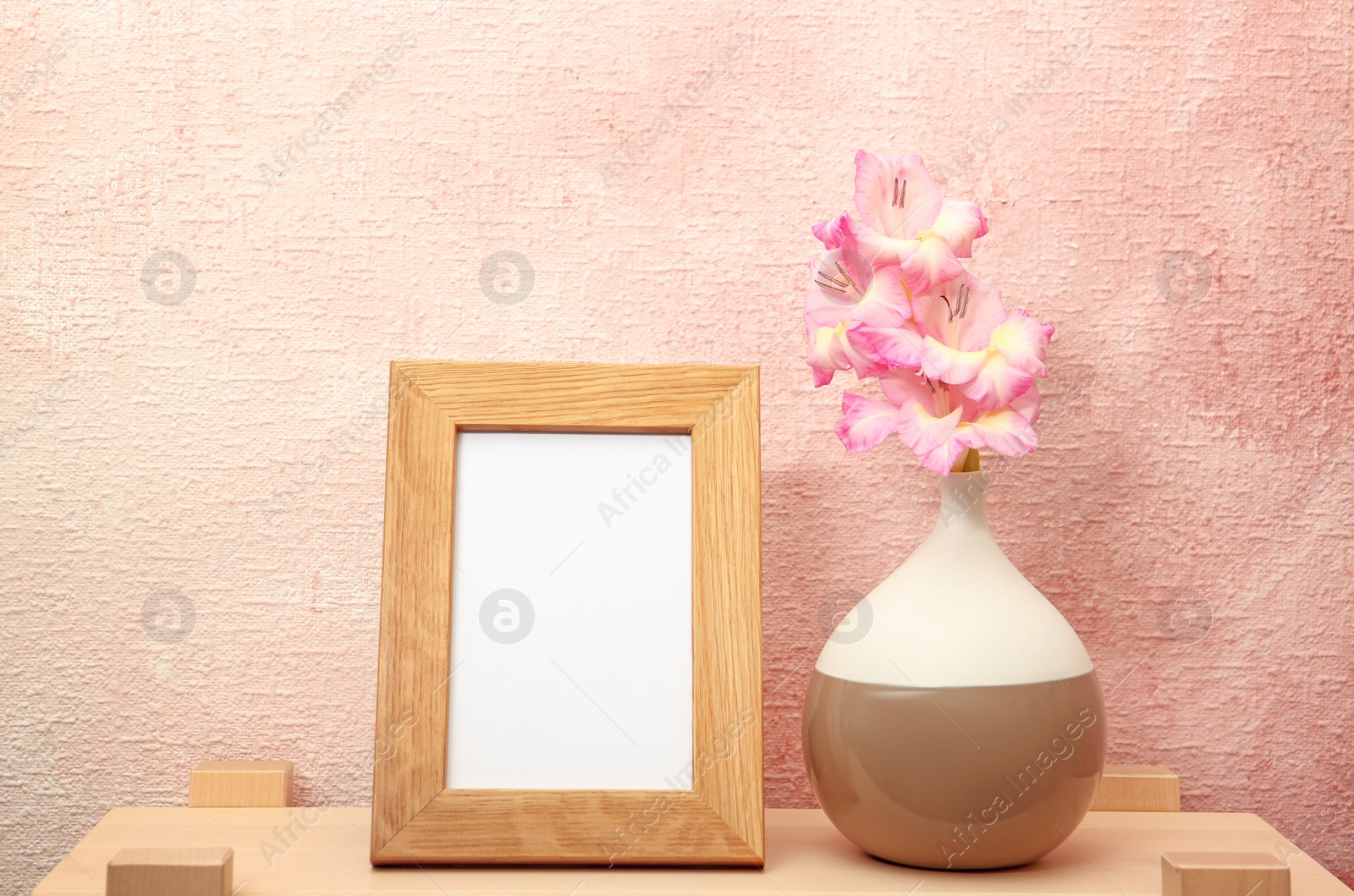 Photo of Blank frame and vase with flowers on table near color wall. Mock up for design