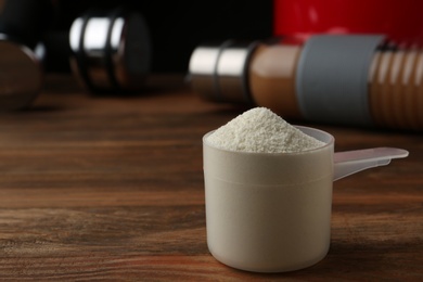 Photo of Measuring scoop of protein powder on wooden table, closeup. Space for text