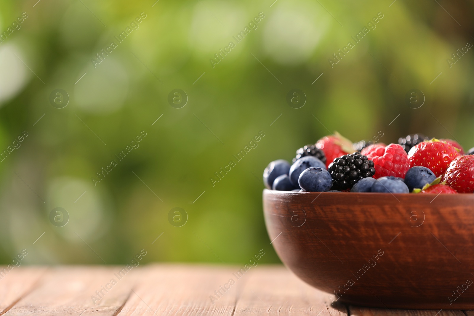 Photo of Bowl with different fresh ripe berries on wooden table outdoors, space for text