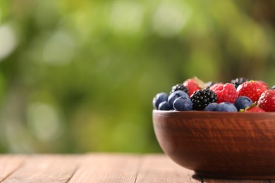 Bowl with different fresh ripe berries on wooden table outdoors, space for text