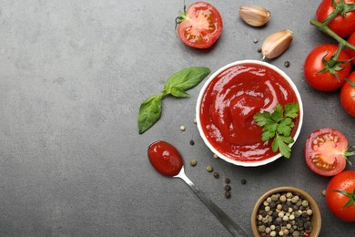 Photo of Delicious tomato ketchup in bowl, spices and products on grey textured table, flat lay. Space for text