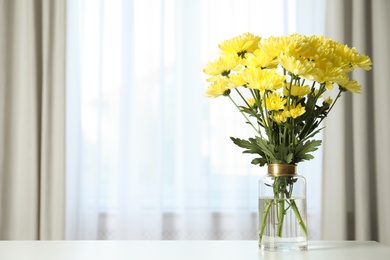 Photo of Vase with beautiful yellow chrysanthemum flowers on table near window indoors, space for text. Stylish element of interior design
