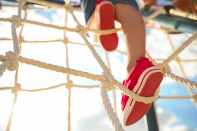 Photo of Child on playground rope climber outdoors, closeup. Summer camp