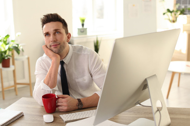 Young businessman with cup of drink relaxing at table in office during break