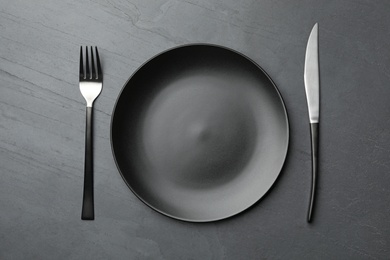 Photo of Stylish ceramic plate and cutlery on dark background, flat lay