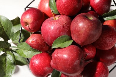 Ripe red apples with water drops and green leaves on white table, flat lay