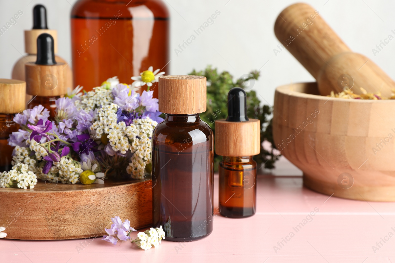 Photo of Aromatherapy. Different essential oils, mortar, pestle and flowers on pink wooden table