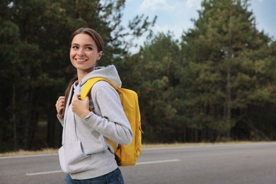 Happy young woman with backpack on road near forest