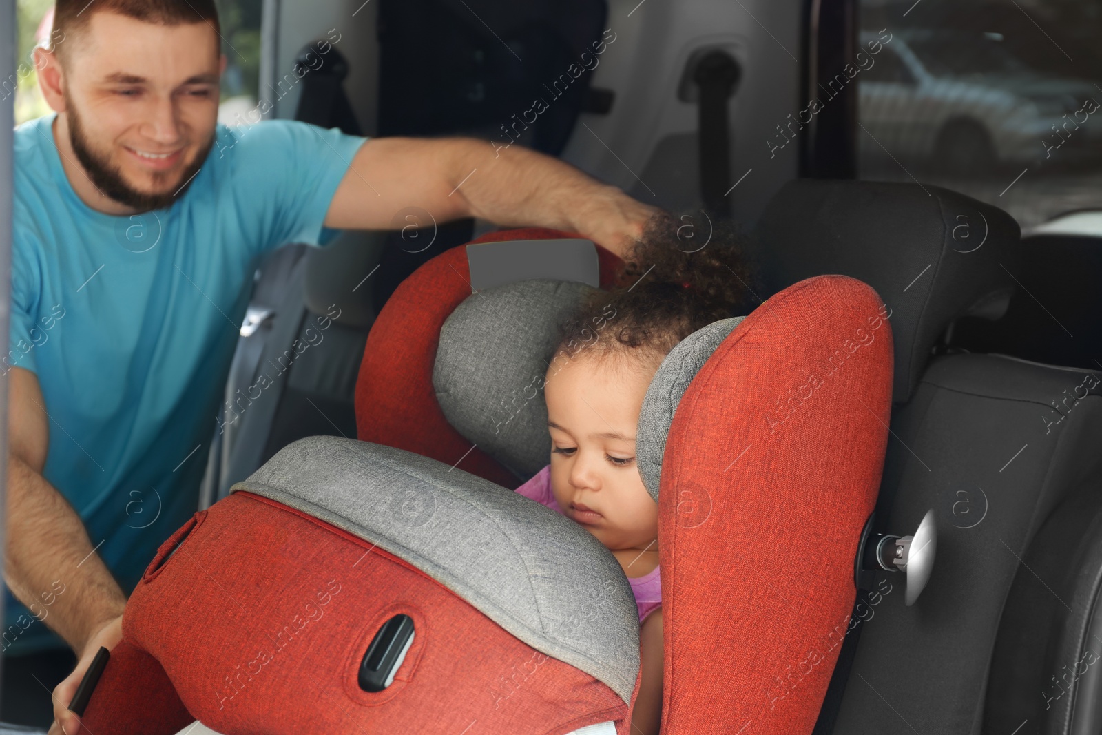 Photo of Father fastening baby to child safety seat inside of car