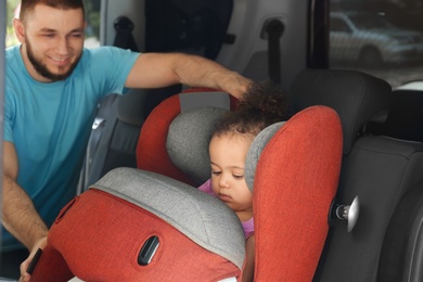 Father fastening baby to child safety seat inside of car