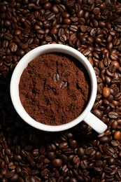 Cup with ground coffee on roasted beans, top view