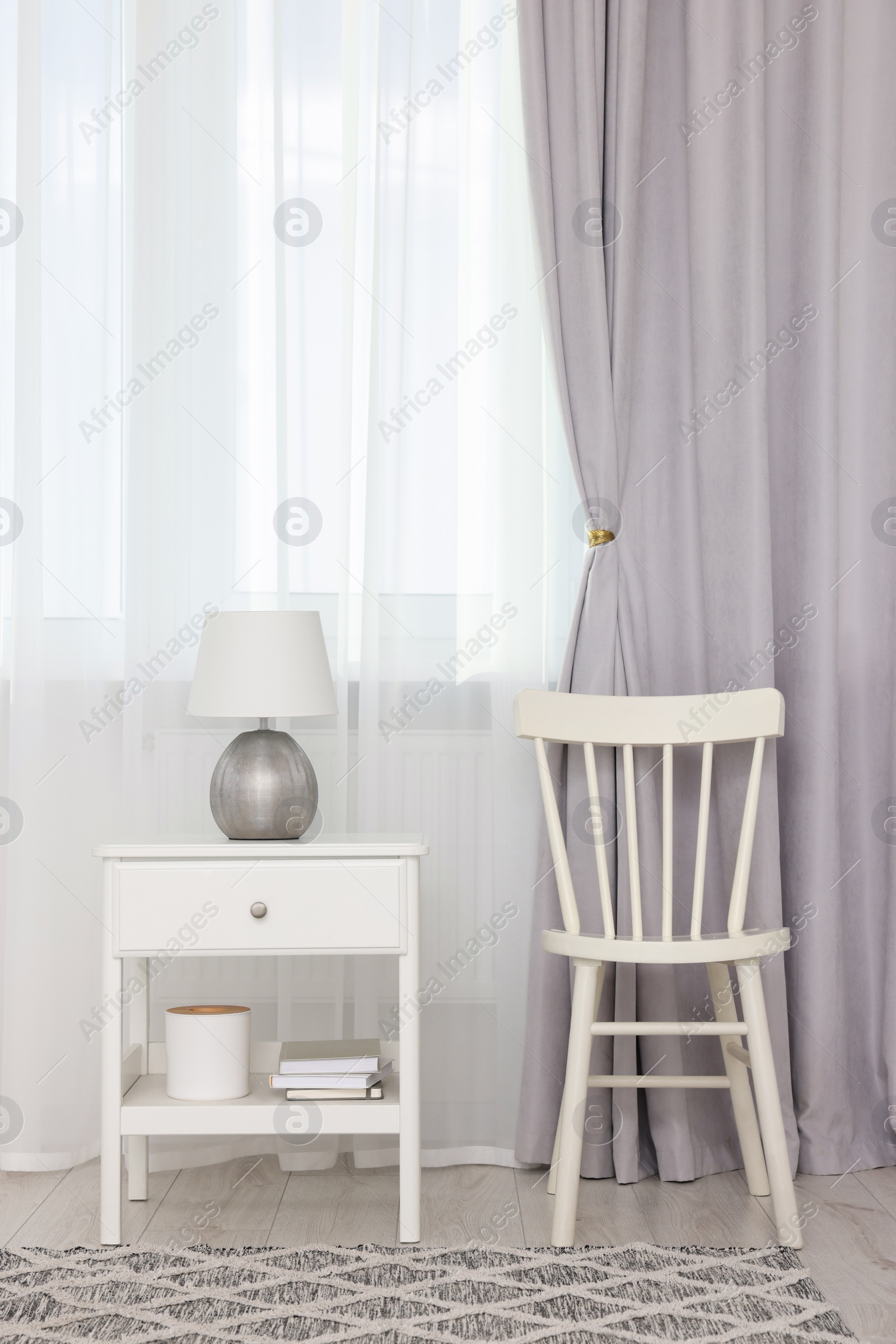 Photo of Stylish room interior with comfortable chair, table and beautiful window curtains