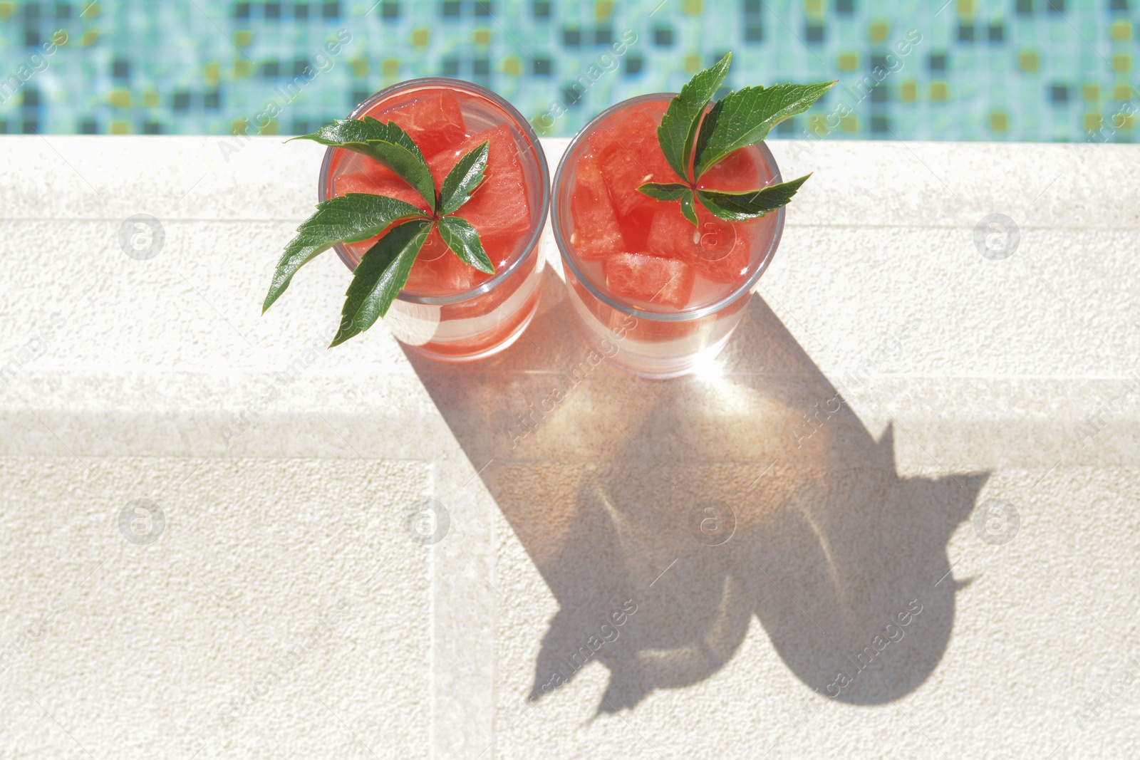 Photo of Refreshing watermelon drink in glasses near swimming pool outdoors, top view. Space for text