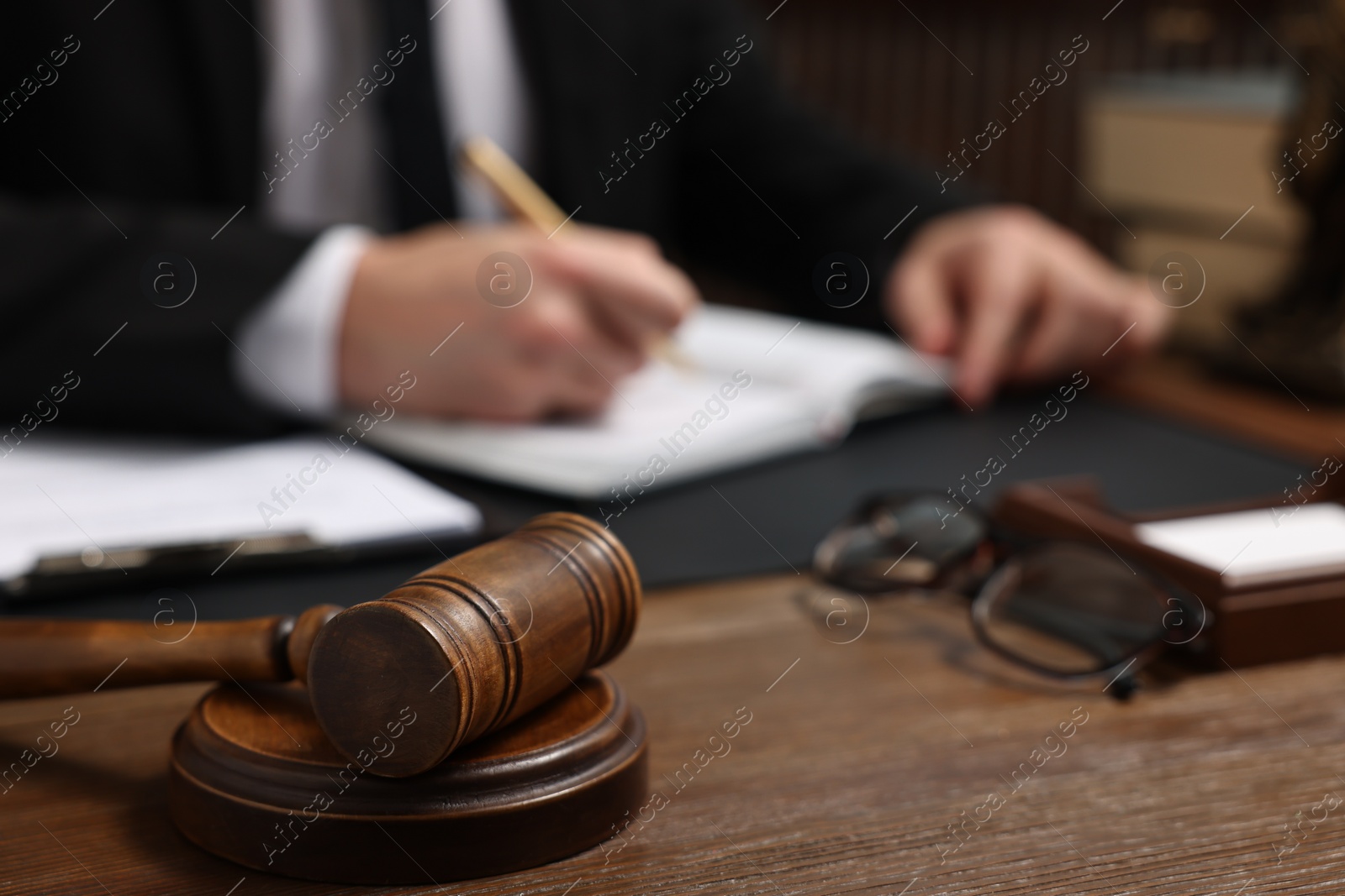 Photo of Lawyer taking notes at wooden table, focus on gavel