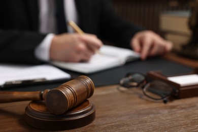 Photo of Lawyer taking notes at wooden table, focus on gavel