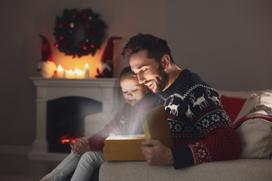 Image of Father and his cute daughter opening gift box with magical light at home. Christmas celebration