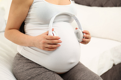 Photo of Pregnant woman with headphones at home, closeup