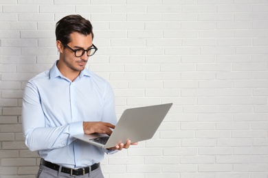Young male teacher with glasses and laptop near brick wall. Space for text