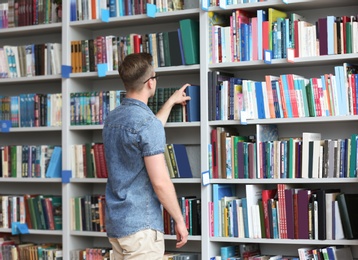 Photo of Young man taking book from shelving unit in library. Space for text