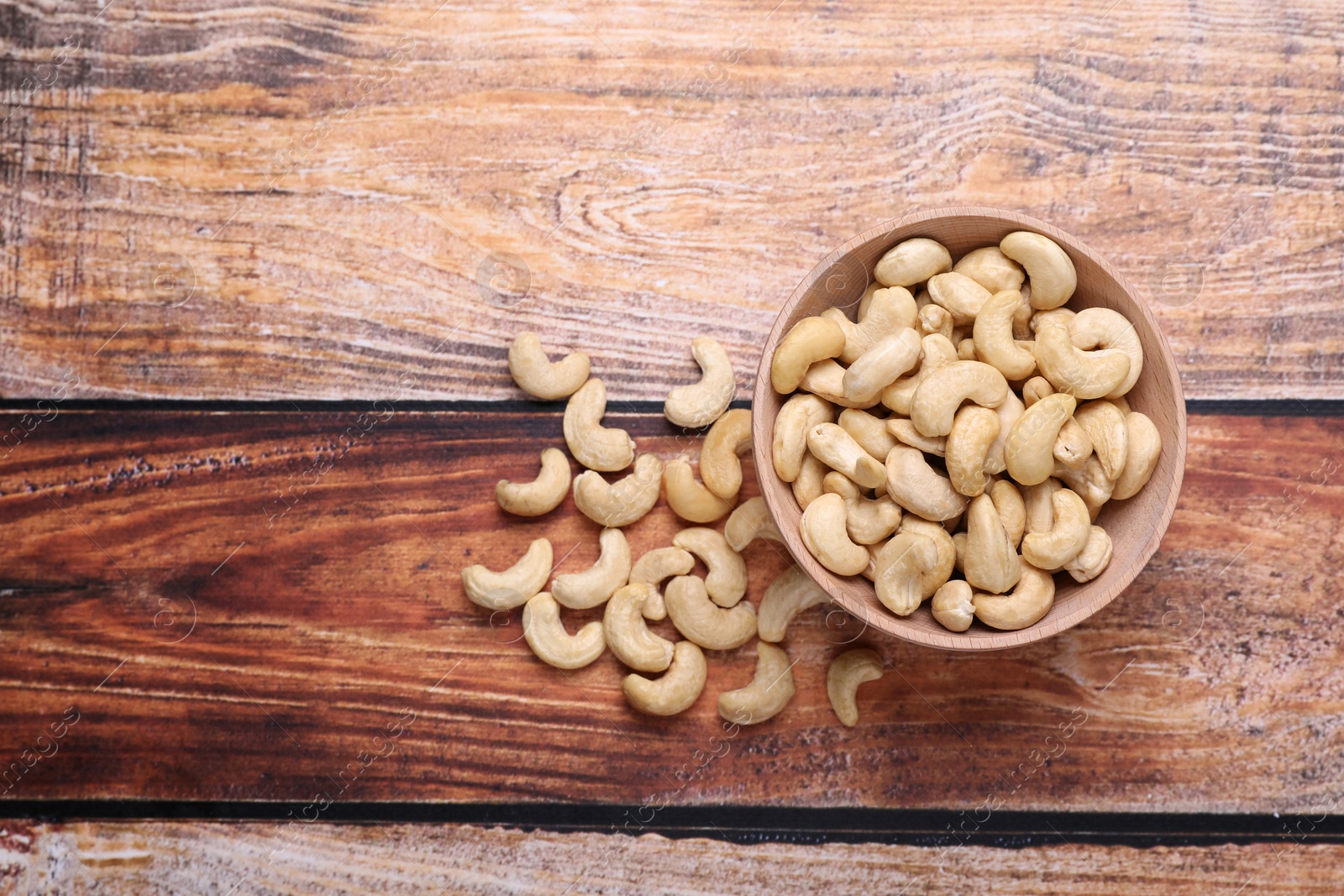 Photo of Tasty cashew nuts in bowl on wooden table, top view. Space for text