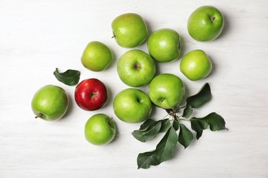 Photo of Red apple among green ones on wooden background, top view. Be different