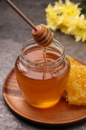 Photo of Pouring sweet golden honey from dipper into jar at grey table