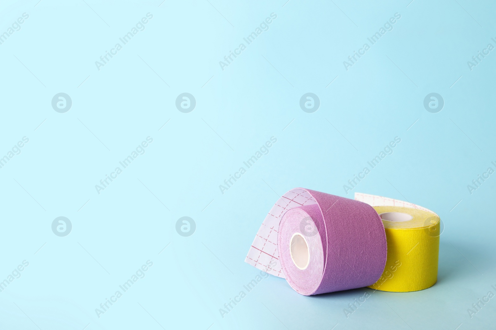 Photo of Bright kinesio tape in rolls on light blue background. Space for text