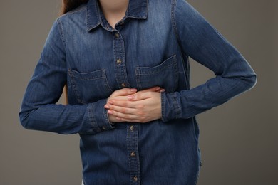Photo of Woman suffering from stomach pain on grey background, closeup