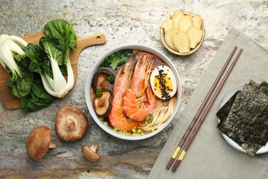 Photo of Delicious ramen with shrimps, ingredients and chopsticks on grey textured table, flat lay. Noodle soup