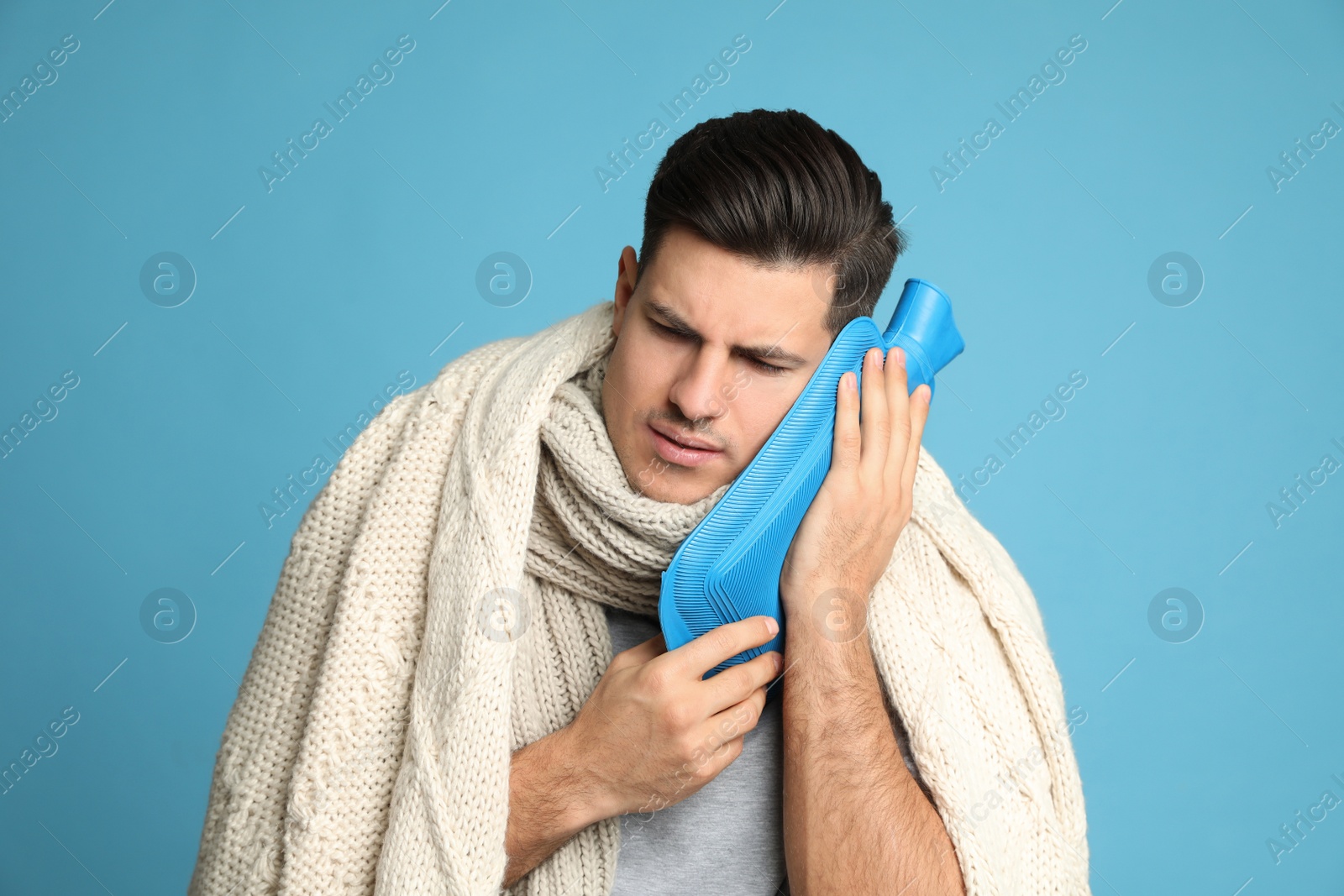 Photo of Ill man with hot water bottle suffering from cold on light blue background