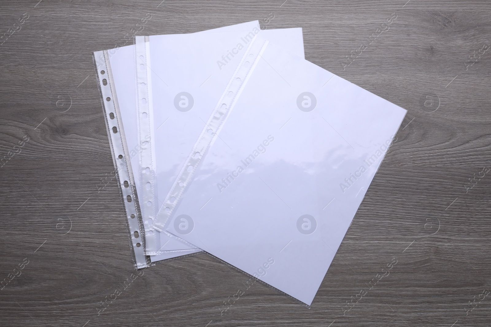 Photo of Punched pockets with paper sheets on wooden table, flat lay