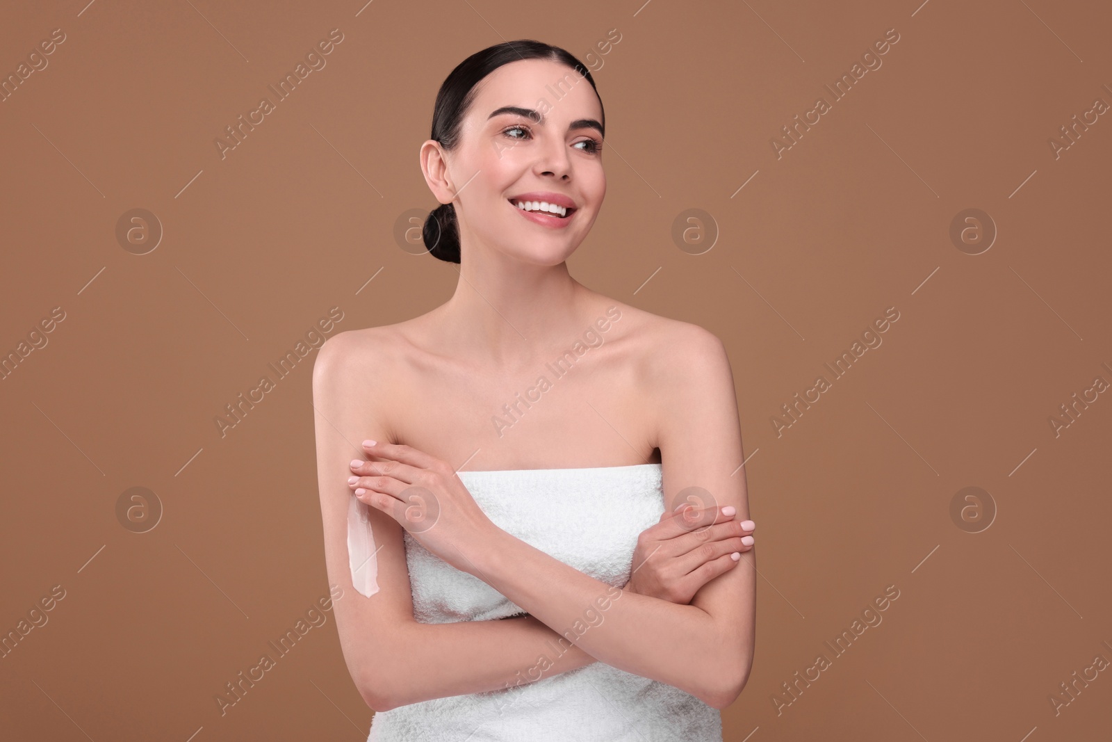 Photo of Beautiful woman with smear of body cream on her arm against light brown background