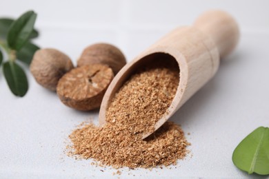 Scoop with grated nutmeg, seeds and green leaves on white table, closeup