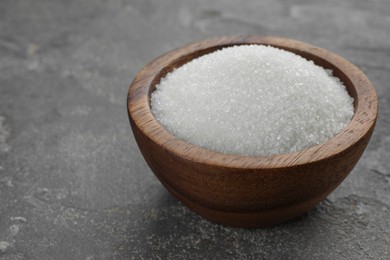 Photo of Granulated sugar in bowl on grey textured table, closeup